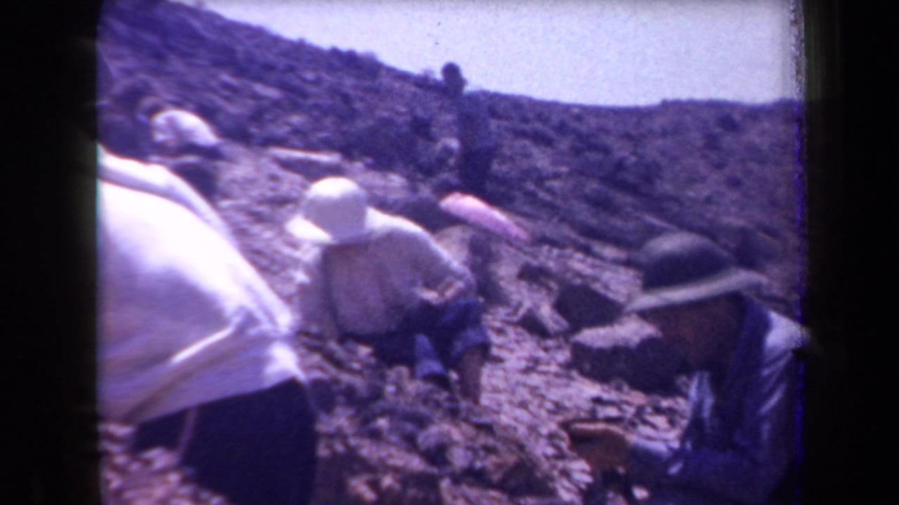 Home-movie frame from Arizona in 1958 showing several adults on a rocky hillside, some crouched as if inspecting the ground.