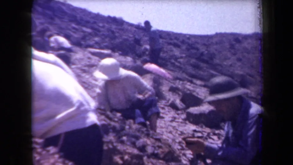 Home-movie frame from Arizona in 1958 showing several adults on a rocky hillside, some crouched as if inspecting the ground.