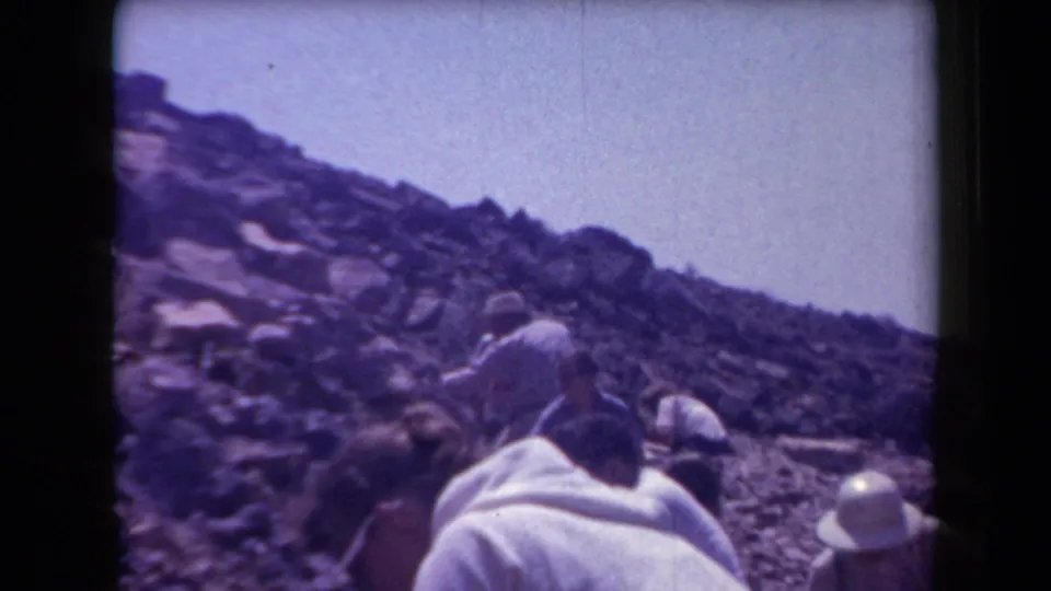 Faded 8mm frame from 1958 Arizona showing adults on a rugged hillside, with one figure leaning forward near the foreground.