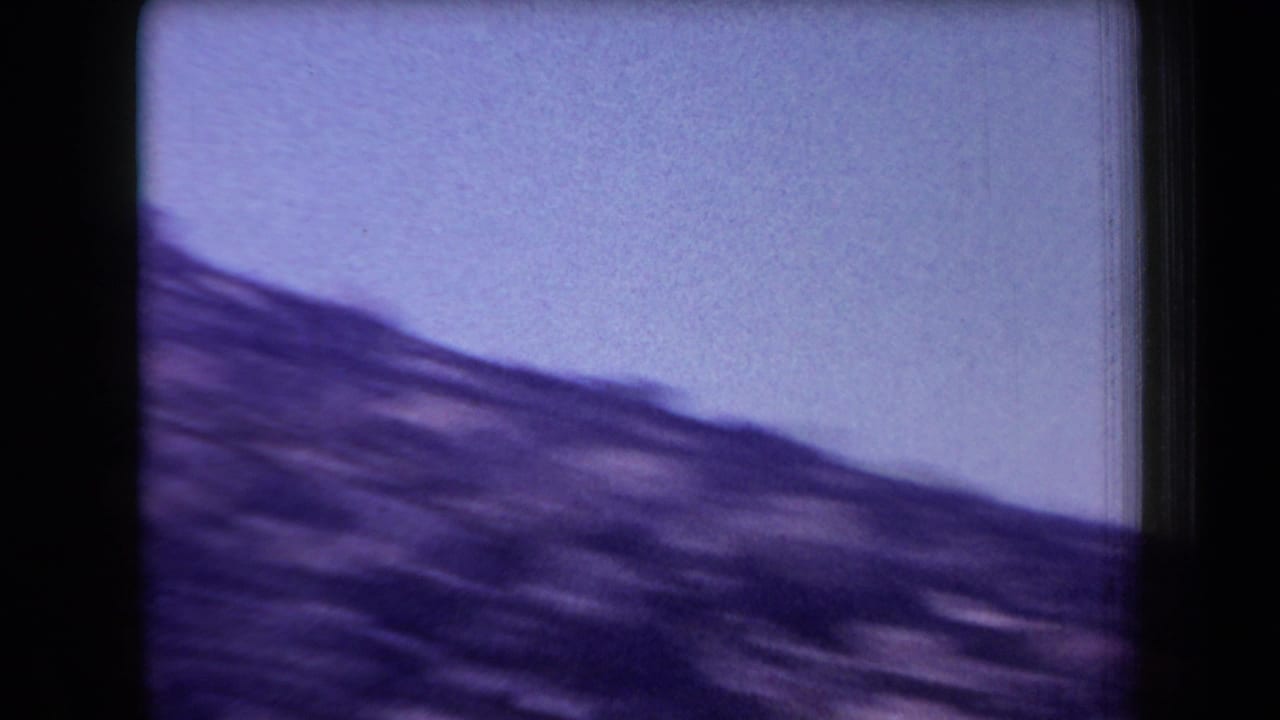 1958 Arizona home-movie frame showing a blurred rocky hillside beneath a hazy purple-tinged sky.