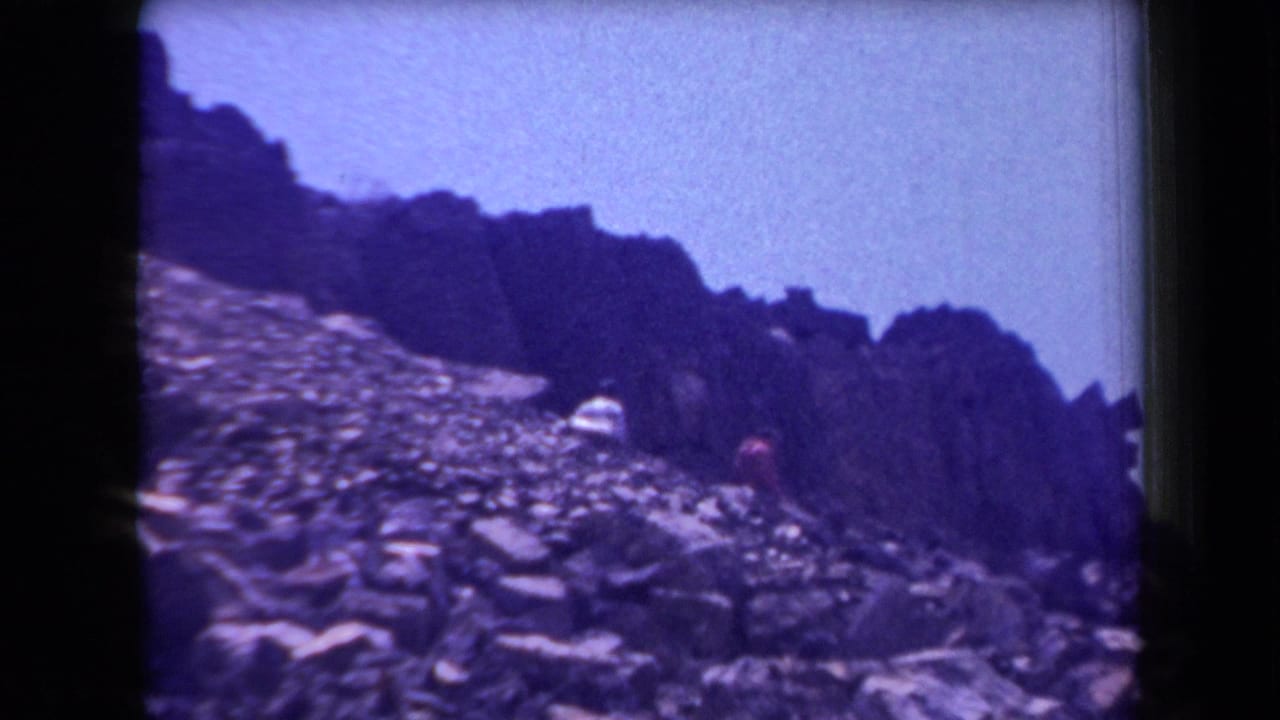 1958 Arizona frame showing small people on a rugged stone slope below dark rocky ridges.