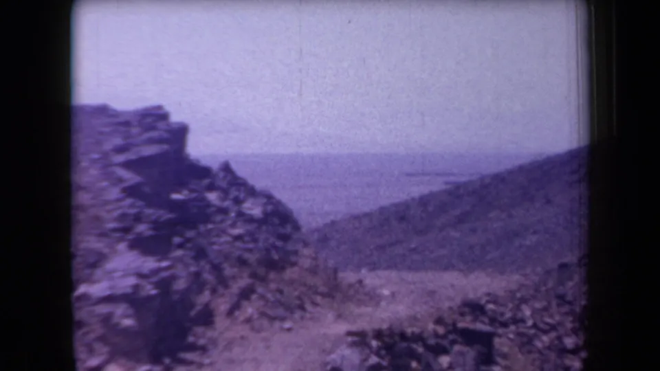 1958 Arizona frame showing a stone outcrop, rough hillside, and hazy open distance in purple-shifted 8mm color.