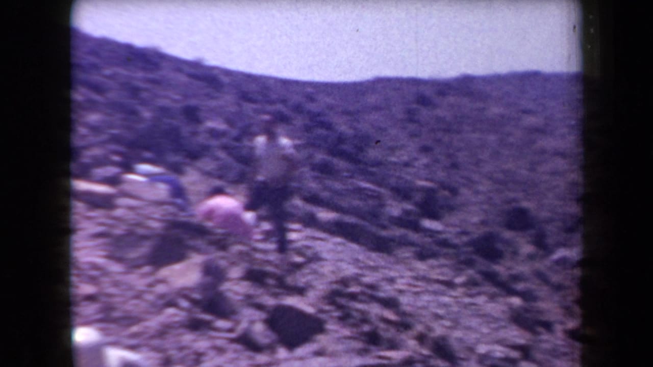 People on a rocky Arizona desert hillside appear to examine or dig around stones in this 1958 home-movie frame.