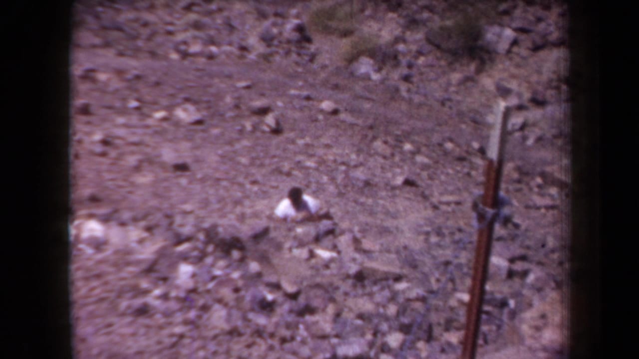 A person in light clothing bends over among rocks near the right edge of the frame.