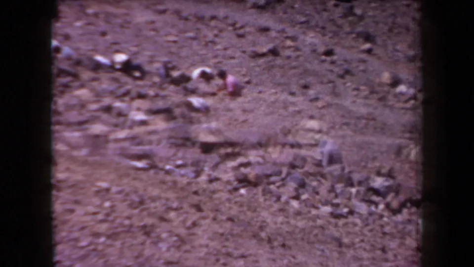 1958 Arizona frame showing multiple distant people bent over in a line across a rocky, arid landscape.