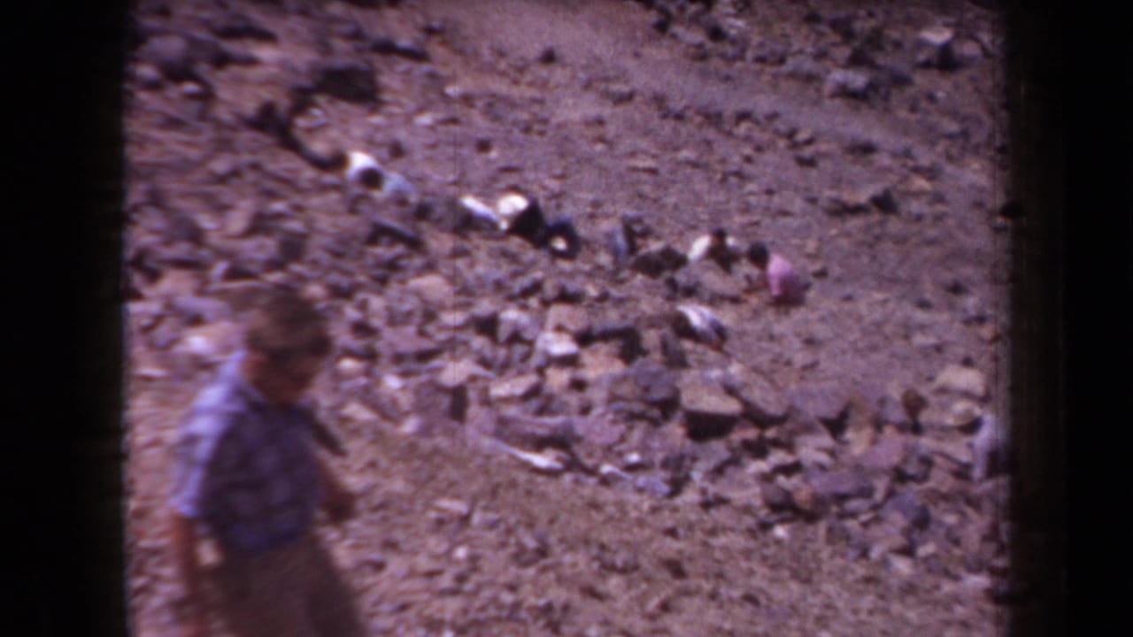 A blurred figure walks past rocky Arizona terrain in 1958 home-movie footage, framed by dark 8mm film edges.