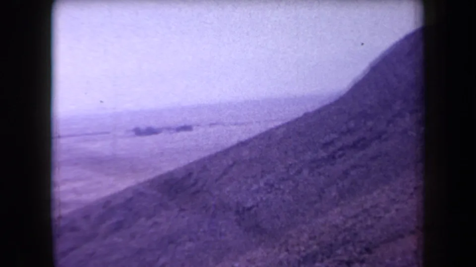 A hazy shoreline or waterline lies below a dark ridge in 1958 Arizona home-movie footage, with purple fading and grain.