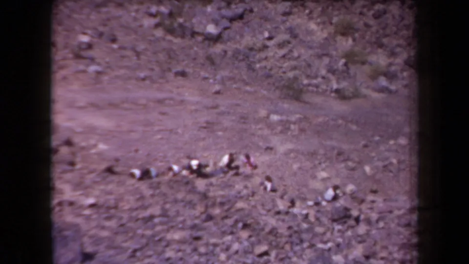 A rugged Arizona rocky hillside fills the frame in color-shifted 1958 8mm footage, with scattered stones across bare ground.