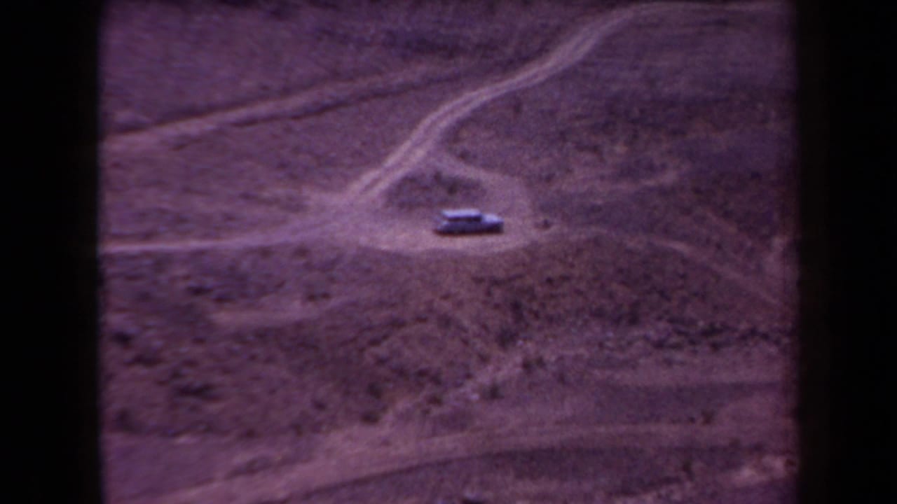 1958 Arizona desert frame with a lone car on an unpaved track, surrounded by branching dirt paths and sparse terrain.