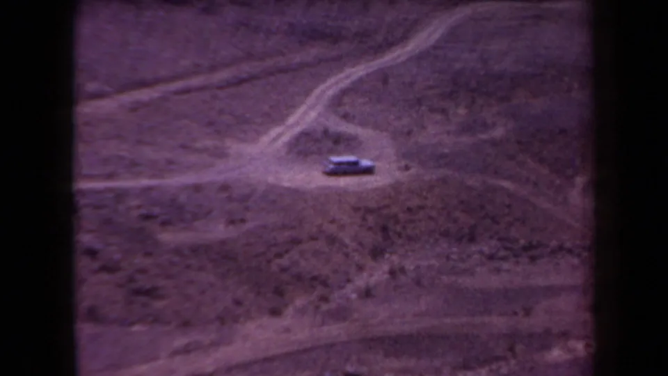 1958 Arizona desert frame with a lone car on an unpaved track, surrounded by branching dirt paths and sparse terrain.