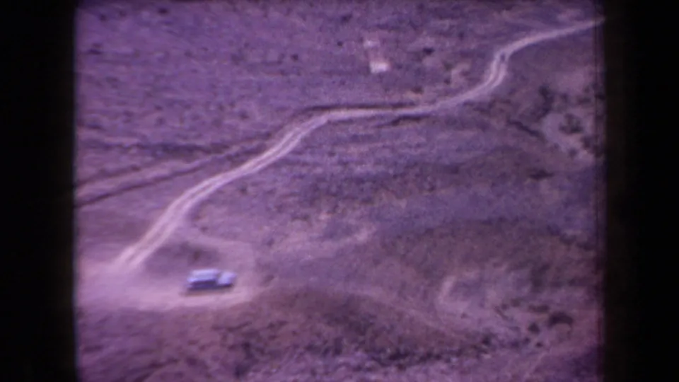 1958 Arizona 8mm frame showing a car low in the frame on a dusty desert road, with winding tracks extending across the landscape.