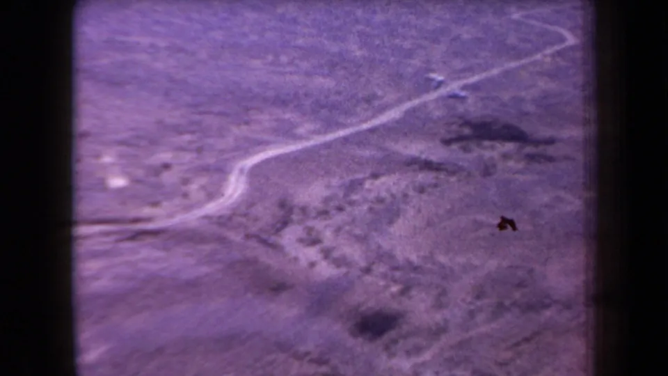 Wide 1958 Arizona desert frame with crossing dirt tracks, rocky arid ground, and a small distant object near the upper trail.