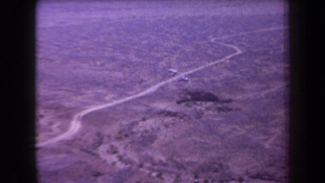 1958 Arizona 8mm frame showing a winding dirt road through sparse, flat desert vegetation with a purple film cast.