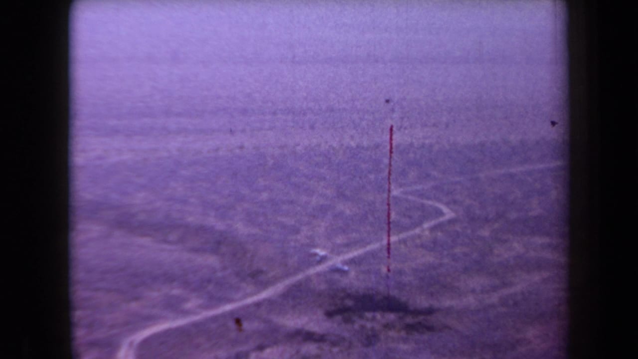 Arizona desert road and sparse brush appear in a 1958 8mm frame marked by grain, purple tint, and a red vertical scratch.