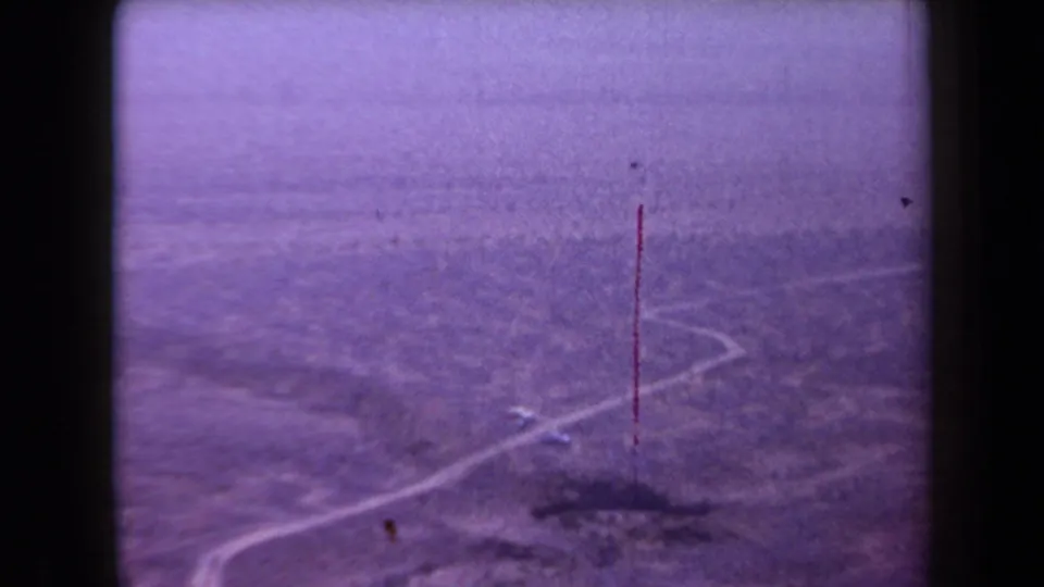 Arizona desert road and sparse brush appear in a 1958 8mm frame marked by grain, purple tint, and a red vertical scratch.