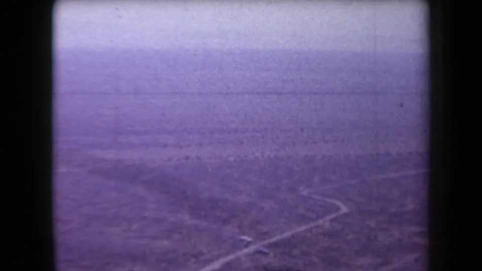 Soft purple-tinted 8mm view of Arizona desert terrain, with a pale winding road receding through sparse vegetation.