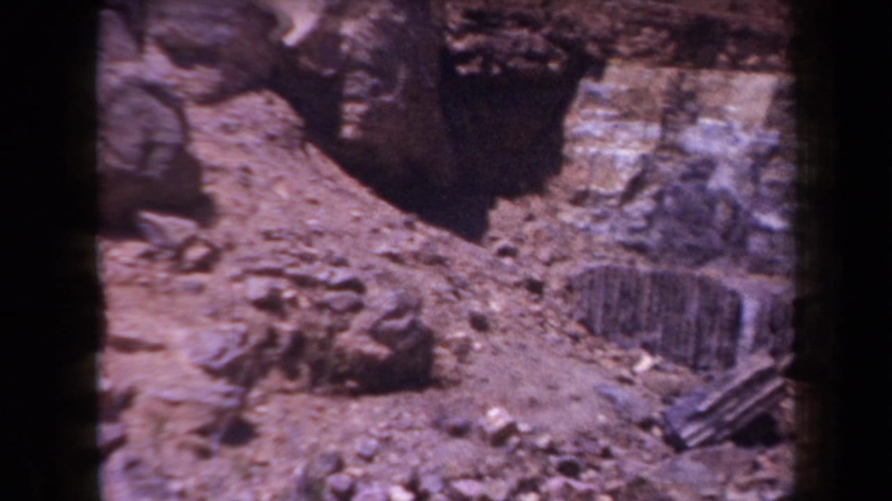 1958 Arizona home-movie frame showing rocky terrain, a dark stone ledge, loose rubble, and a weathered wood piece near the ground.