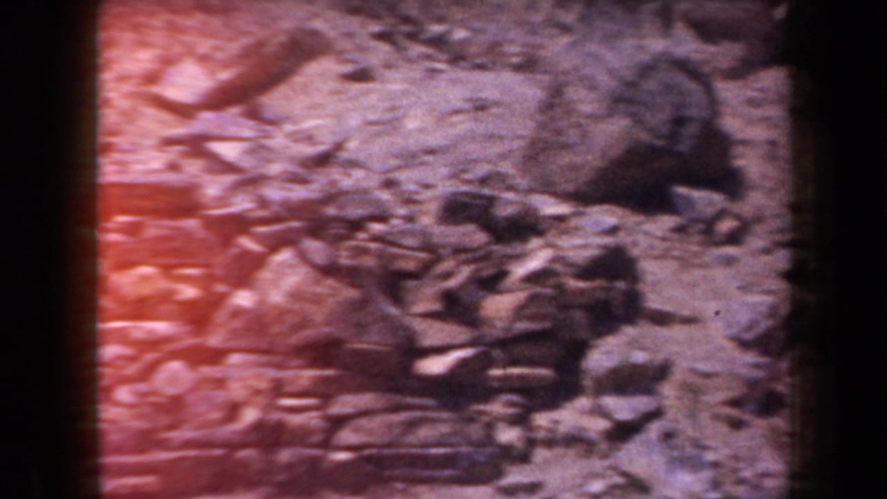 Loose rocks and rubble on uneven terrain with reddish film flare.