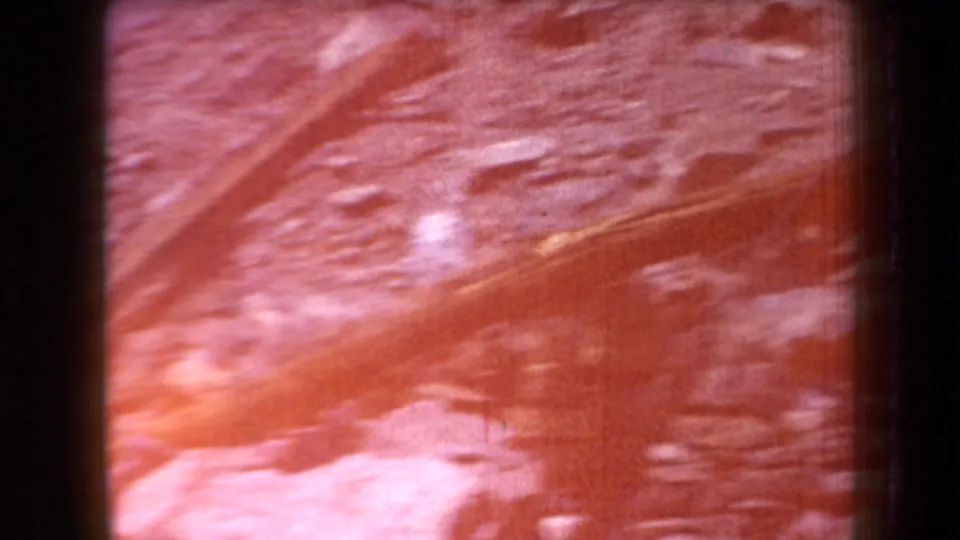 1958 Arizona home-movie frame with blurred stones and ground texture under a strong red-orange exposure flare.