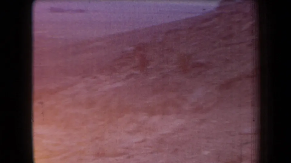 1958 Arizona home-movie frame showing a hazy sloped landscape with muted rocky ground and faded purplish color.