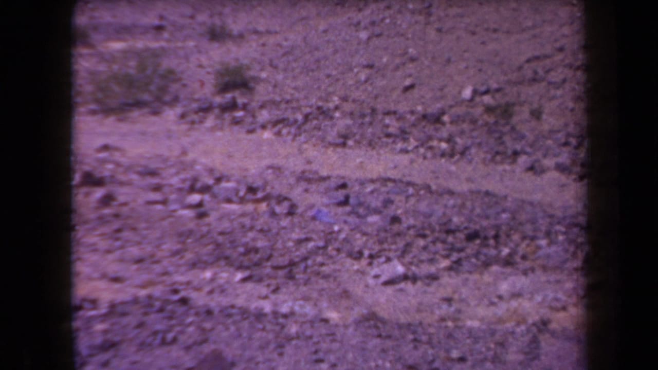 1958 Arizona 8mm frame showing barren rocky ground, scattered scrub, and harsh sunlight before any visible smoke burst.