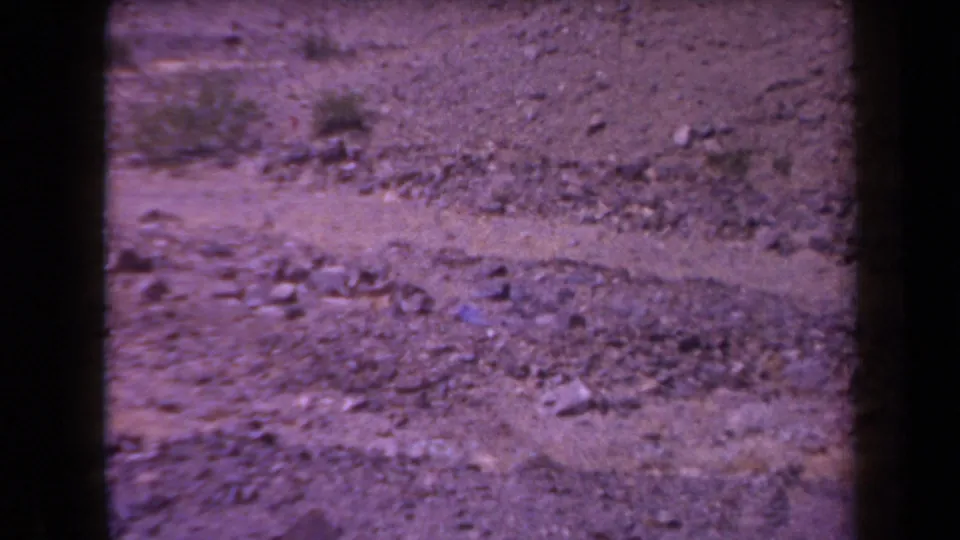 1958 Arizona 8mm frame showing barren rocky ground, scattered scrub, and harsh sunlight before any visible smoke burst.