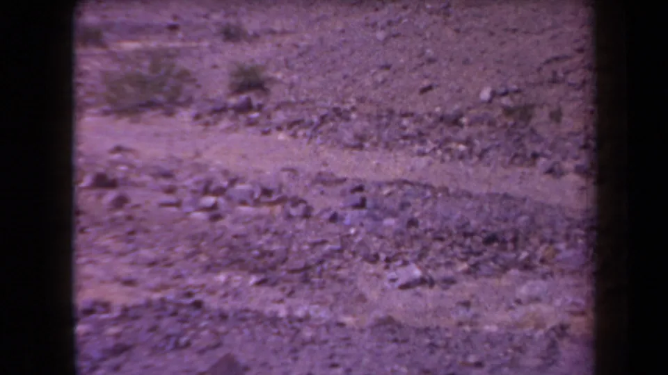 1958 Arizona 8mm view of rocky desert soil and sparse vegetation, with no people or structures visible.