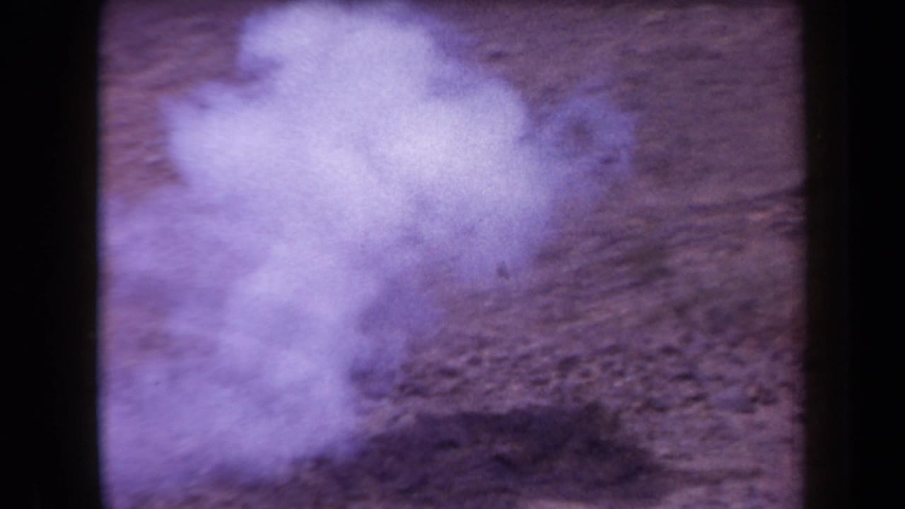 Hazy 1958 Arizona 8mm frame showing rocky desert ground with strong purple color fading and no clearly visible people.