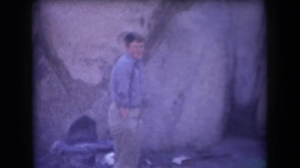 A man in a light blue shirt and khaki pants stands near a rough stone wall in the final 1958 Arizona home-movie frame.