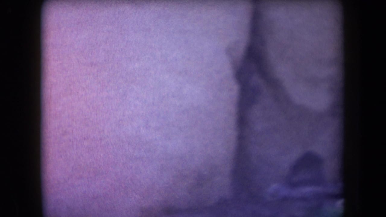 Faded 1958 Arizona 8mm frame with very soft focus, dark border, and barely visible outdoor shapes.