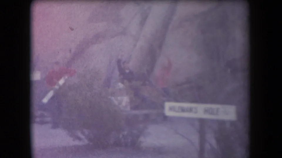 1958 Arizona home-movie frame with a small group near the Hileman's Hole sign and two red-clad figures in the brush.