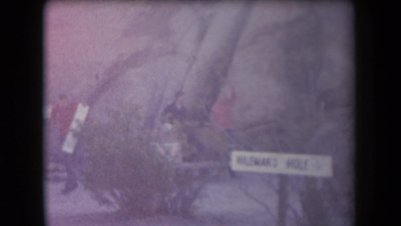 1958 Arizona home-movie frame showing people near a rocky outdoor site and a sign that appears to read Hileman's Hole.