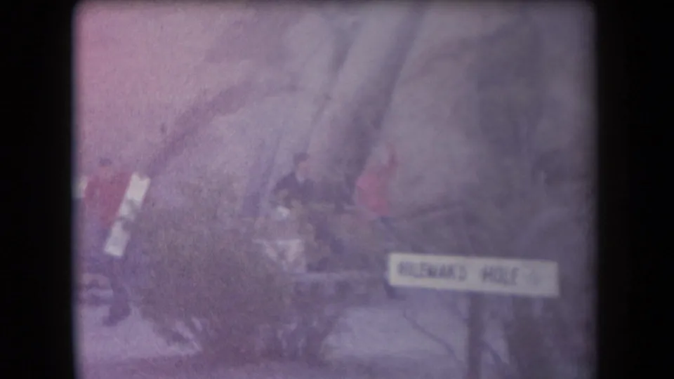 1958 Arizona home-movie frame showing people near a rocky outdoor site and a sign that appears to read Hileman's Hole.