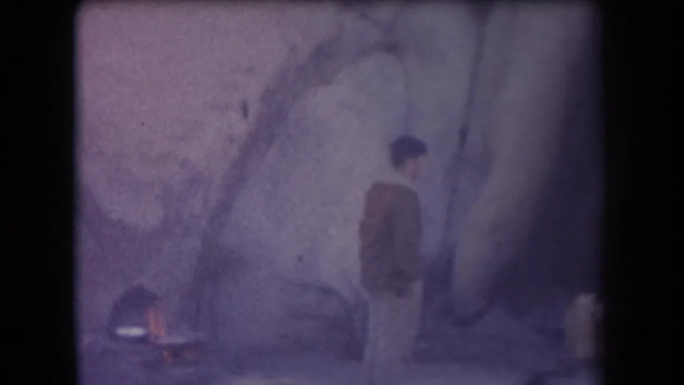1958 Arizona home-movie frame showing a person beside a rocky formation under bare branches, with another figure partly visible.