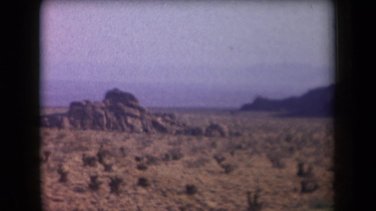 1958 Arizona 8mm frame with a rugged rock formation rising from a sparse desert plain beneath a hazy sky.