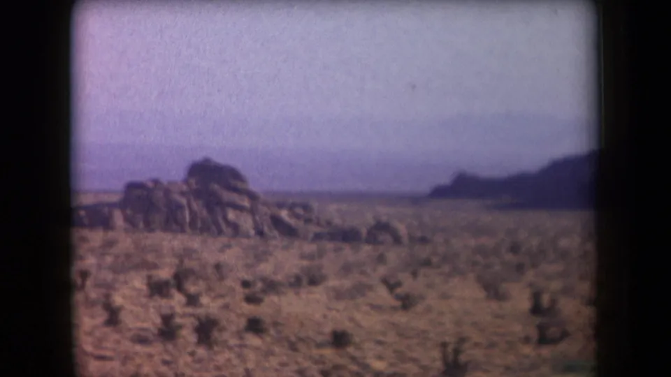1958 Arizona 8mm frame with a rugged rock formation rising from a sparse desert plain beneath a hazy sky.