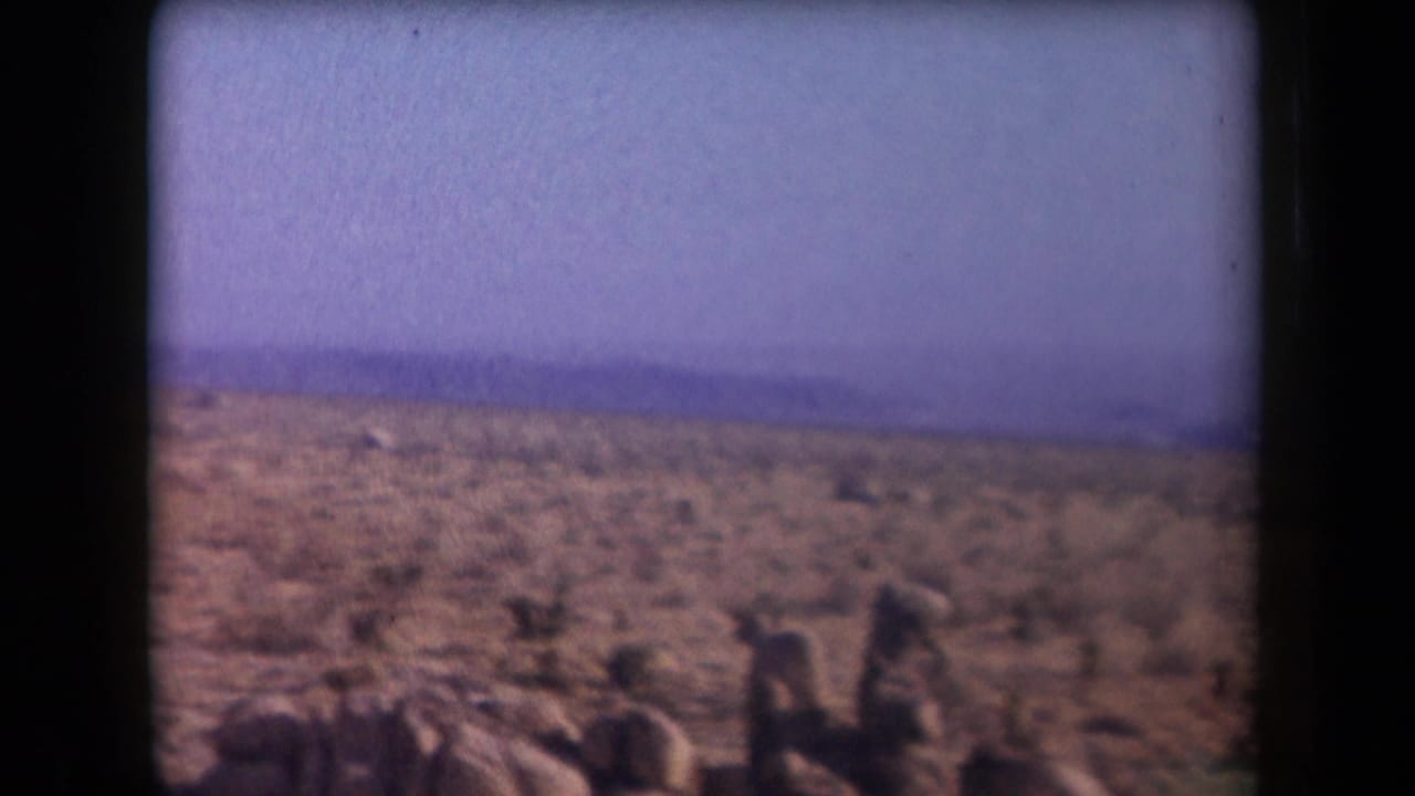 1958 Arizona 8mm frame showing an open desert plain, sparse scrub, low horizon mountains, and visible film gate edges.