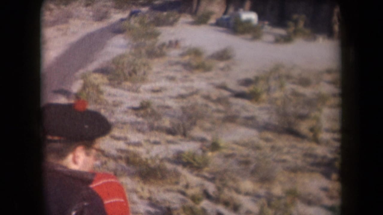1958 Arizona home-movie frame showing two adult men walking near sparse desert shrubs and rocky ground.