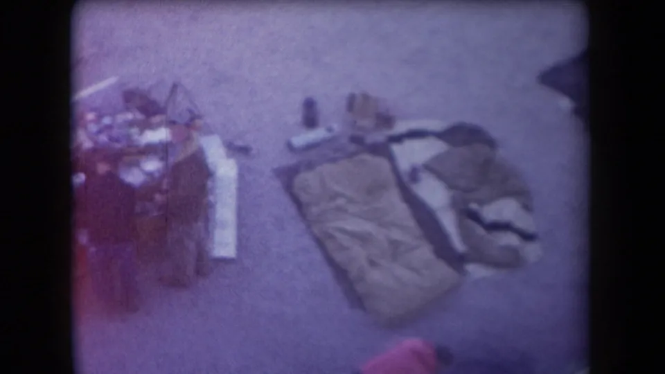 1958 Arizona home-movie frame with sleeping bags, clothing, and small camping items seen from above.