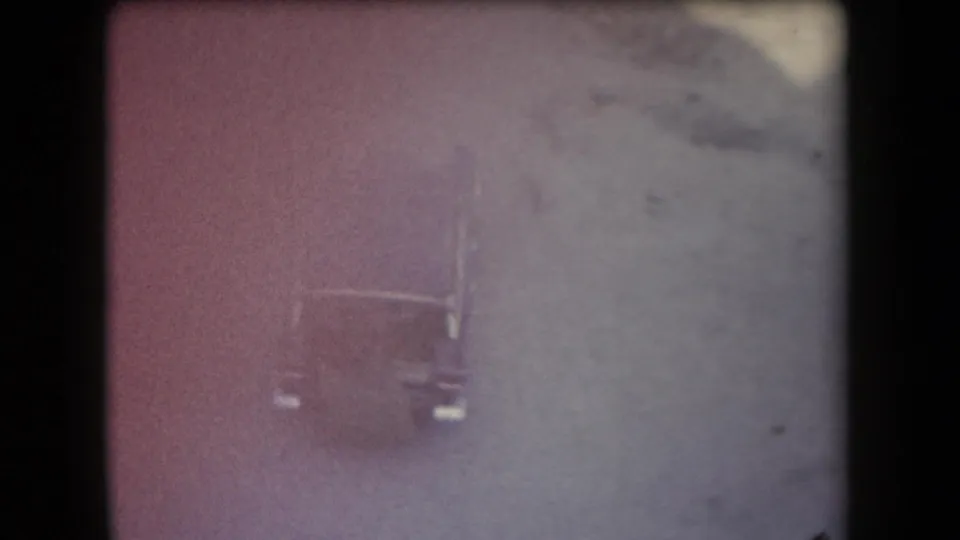 High-angle 1958 Arizona 8mm frame of a dark car on a dusty desert road, softened by faded color and grain.