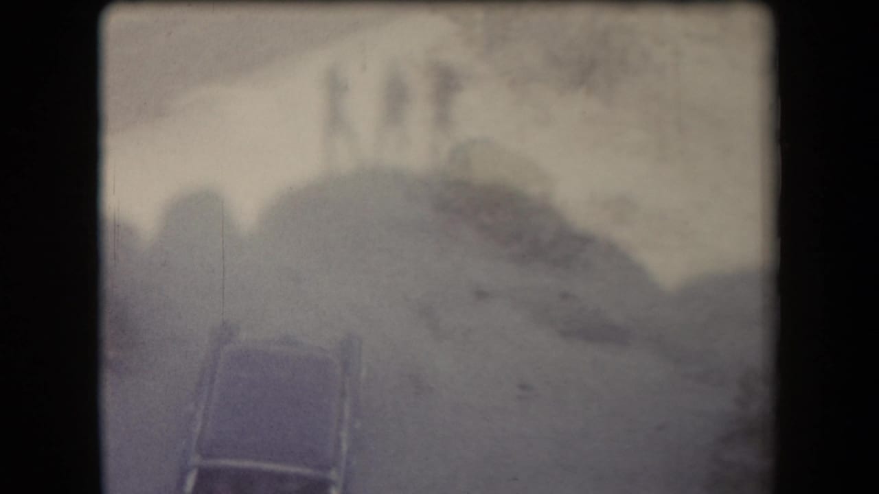 Faded 8mm view of a car below rocky Arizona terrain, with soft focus and heavy edge shadow from the film frame.