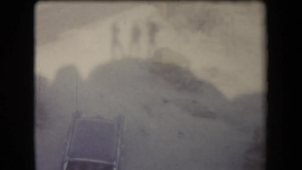 Faded 8mm view of a car below rocky Arizona terrain, with soft focus and heavy edge shadow from the film frame.
