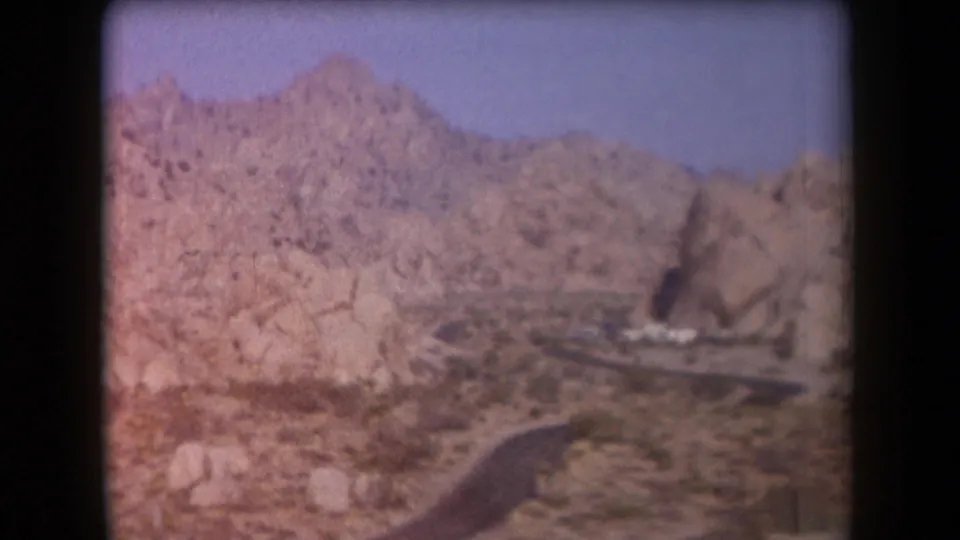1958 Arizona home-movie view of a road bending through arid terrain toward light buildings at the base of rocky hills.