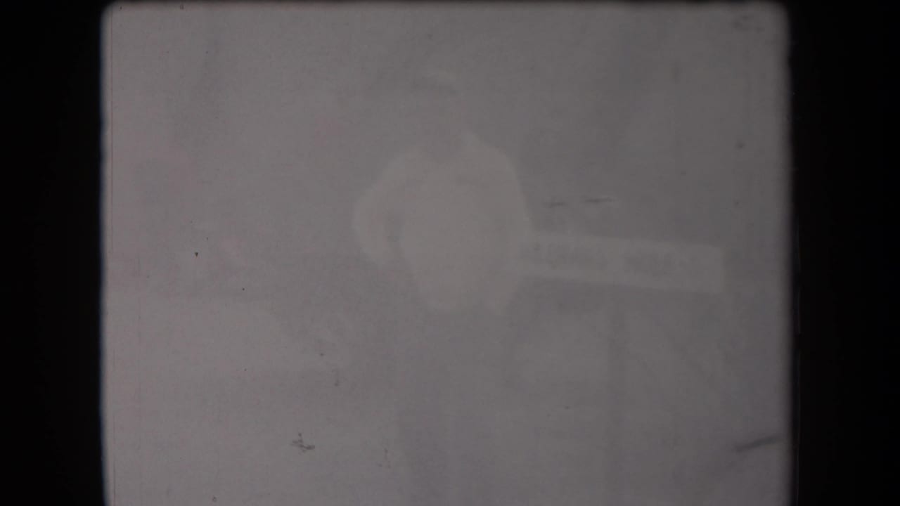 Soft 1958 Arizona home-movie frame with a barely visible adult figure and a washed-out horizontal sign-like object.