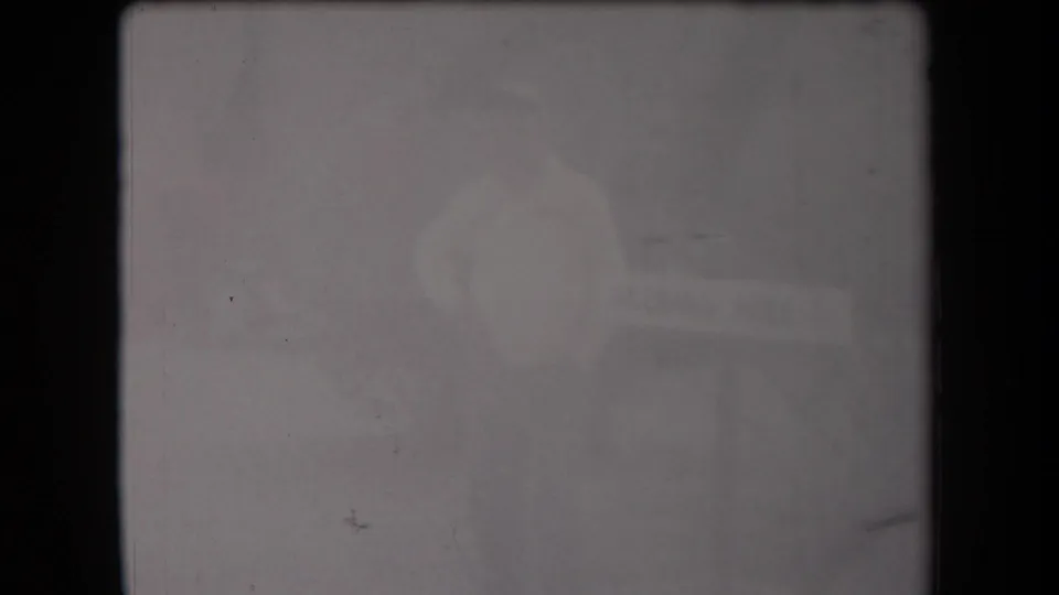 Soft 1958 Arizona home-movie frame with a barely visible adult figure and a washed-out horizontal sign-like object.