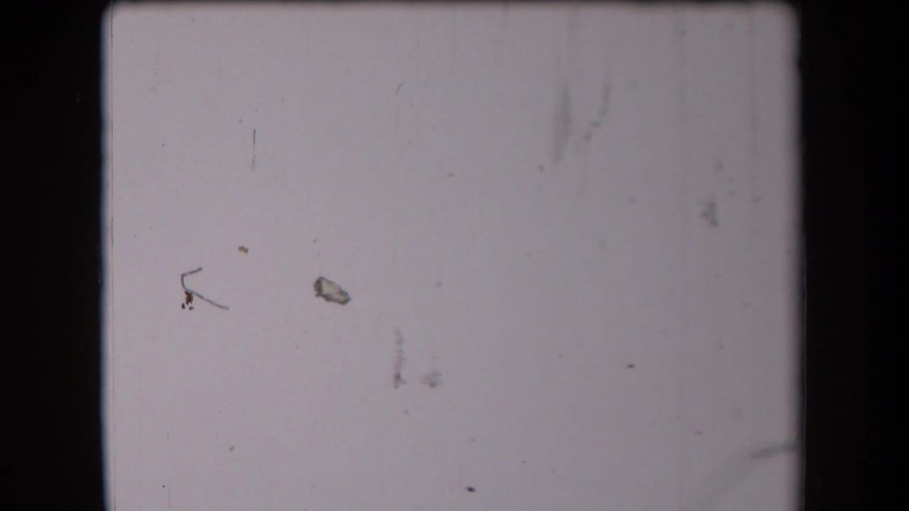 Pale scratched film frame with dust marks and no clear subject visible.