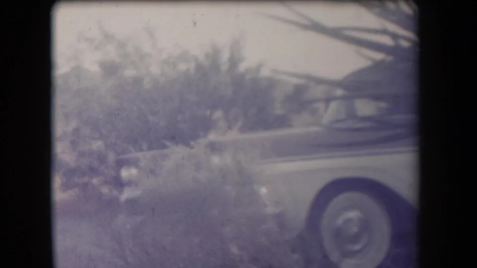 1958 Arizona frame showing part of a vintage car, including a wheel and bodywork, partly obscured by desert plants.