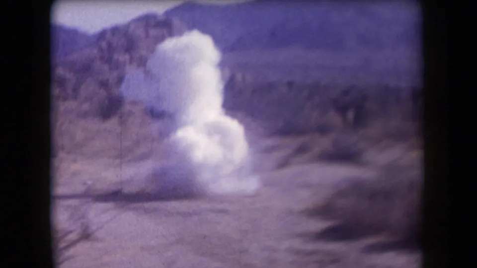1958 Arizona 8mm frame showing a white smoke plume erupting from the desert floor against low hills.
