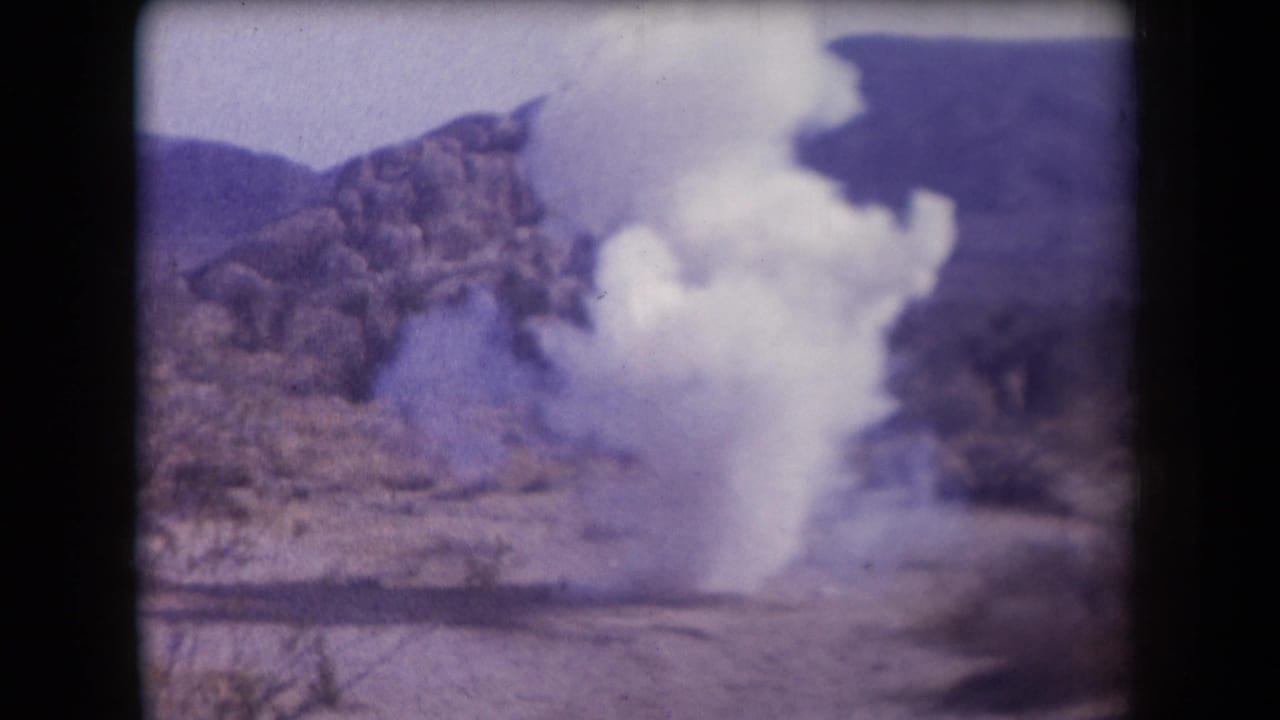1958 Arizona 8mm frame showing a pale smoke or dust plume rising from desert ground below rocky hills.