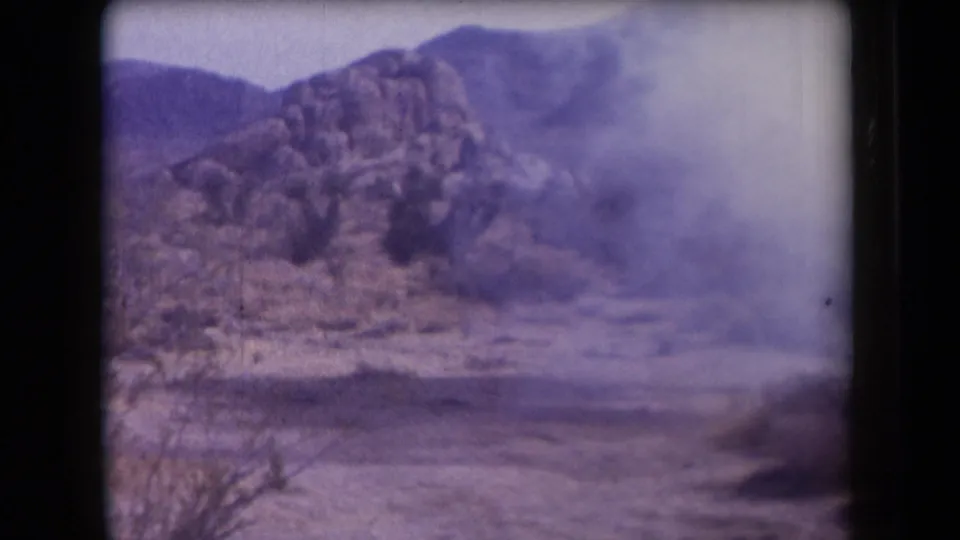 1958 Arizona 8mm frame showing a low, hazy dust or smoke cloud drifting in front of rocky desert terrain.